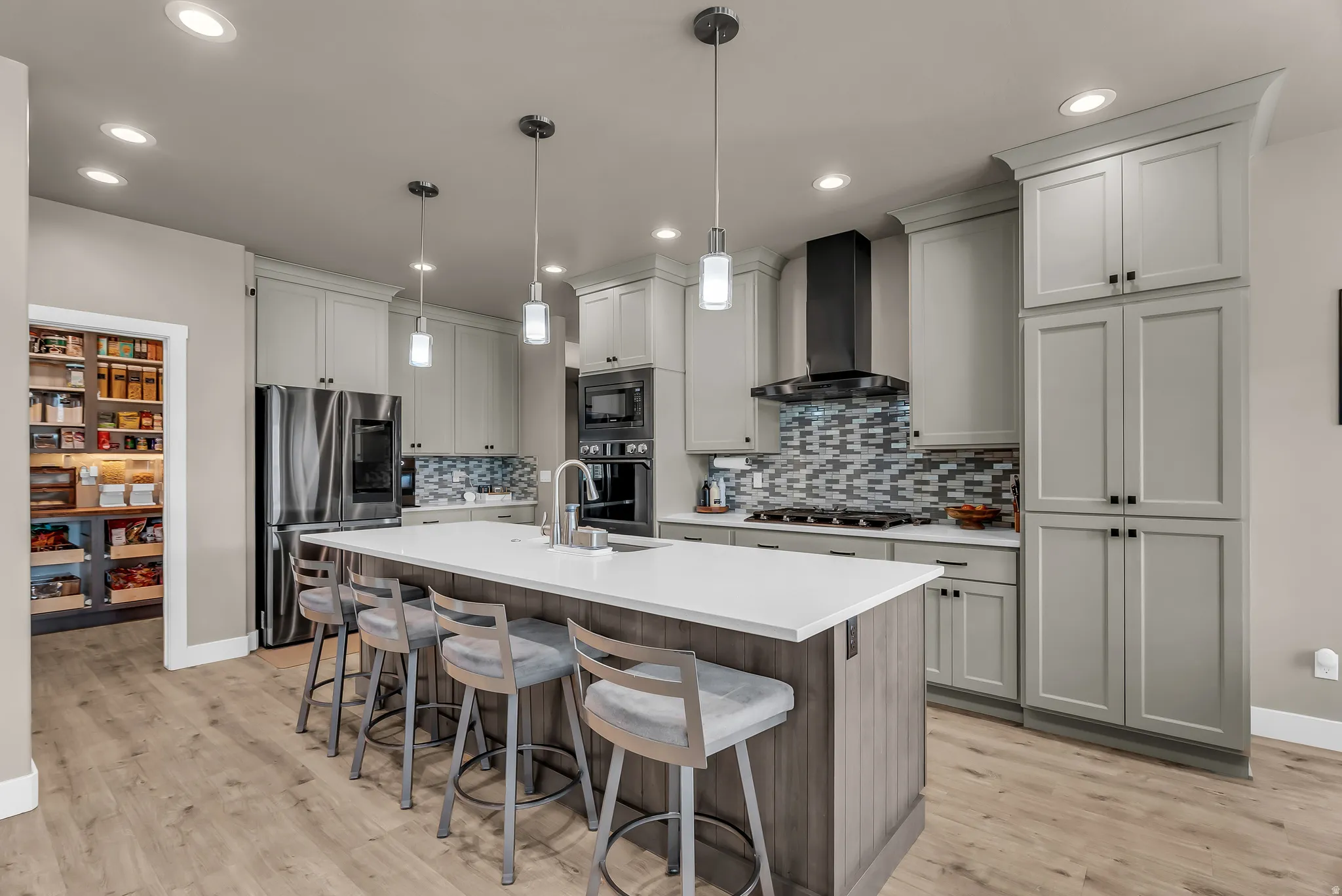 Well-appointed kitchen featuring light-colored cabinetry, stainless steel appliances, a multi-tone tile backsplash, a center island with countertop seating, and wood-finish flooring
