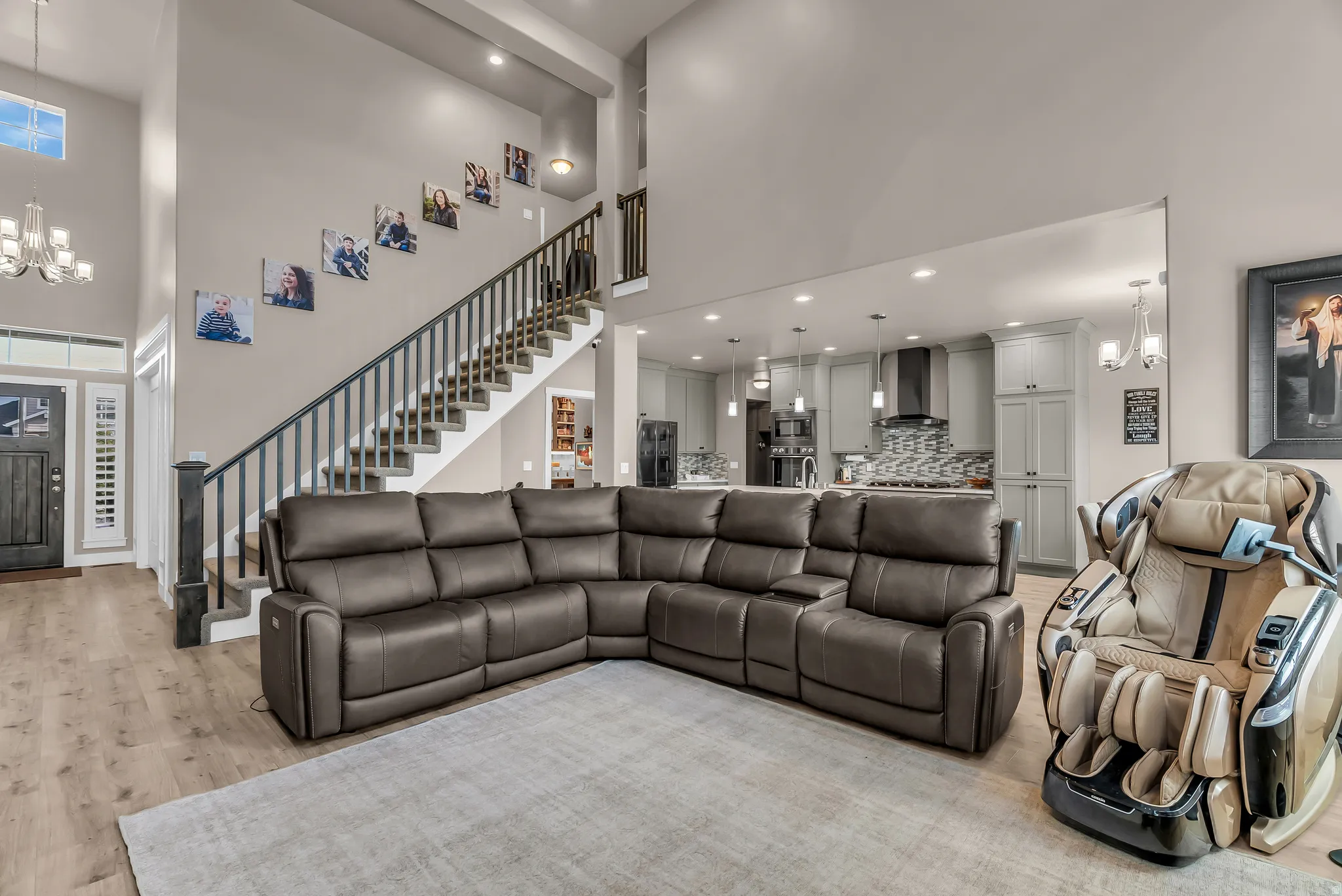 High ceilings, wood-finish flooring, two-story staircase with dark banister, kitchen with light cabinetry and pendant lighting, and a front entry door with transom window