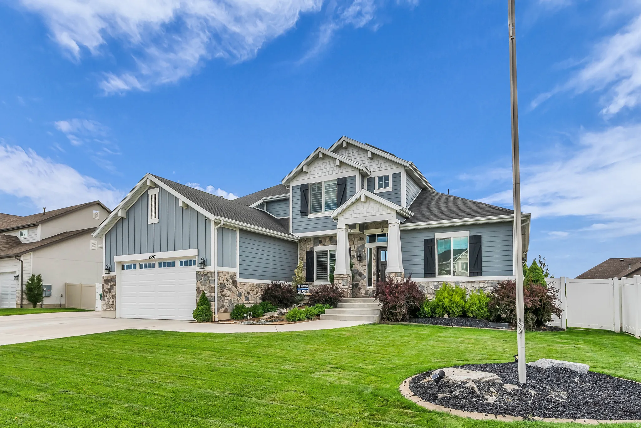 Two-story exterior with mixed siding and stone accents, dual garage doors, a covered front entry with columns, and established landscaping