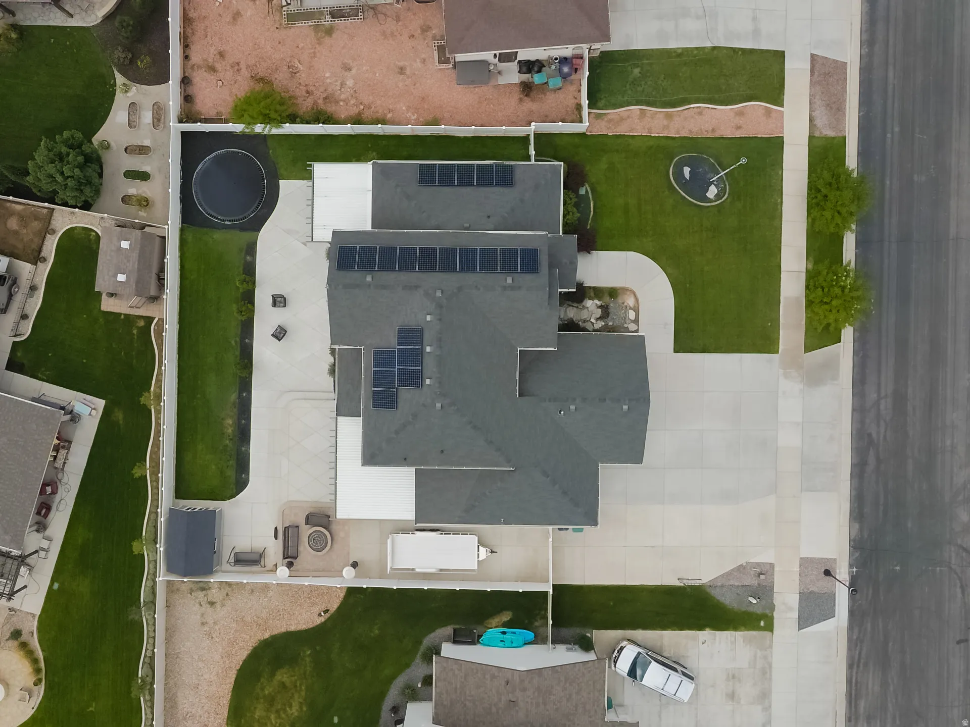 Extensive concrete driveway, multiple solar panel arrays, manicured lawns, and a private backyard patio with a built-in fire pit