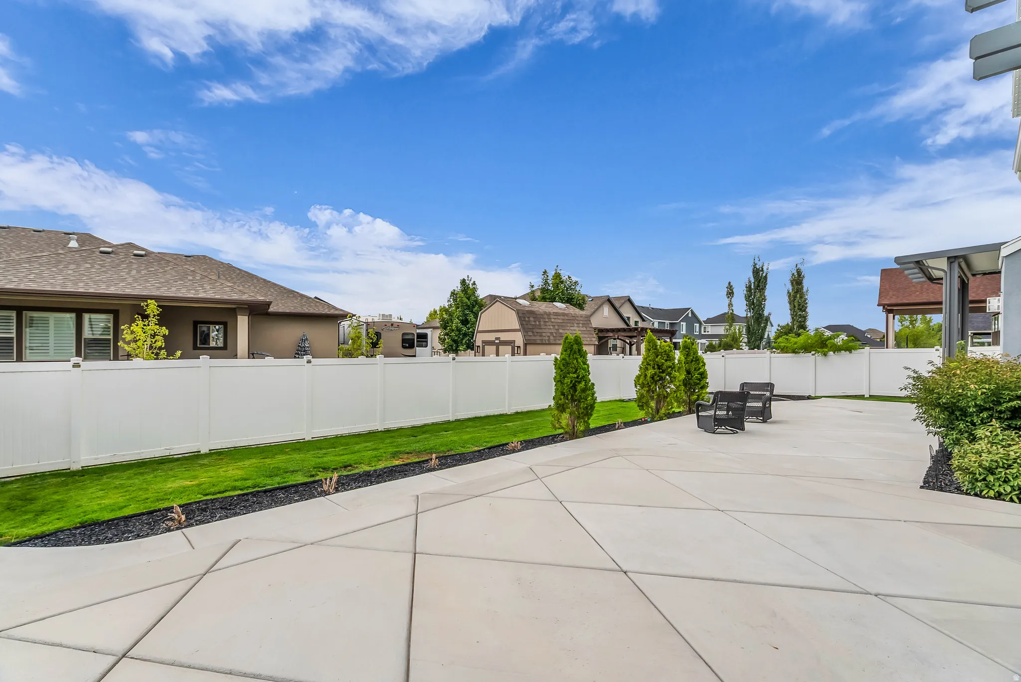 Expansive concrete patio with decorative scoring, bordered by a manicured lawn and a white privacy fence