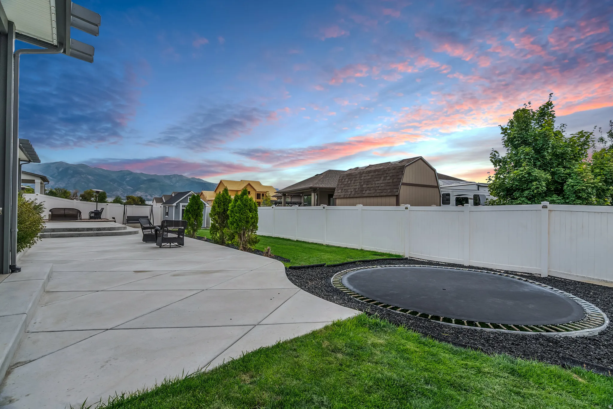 Expansive concrete patio with tiered sections, surrounded by a manicured lawn and a white privacy fence