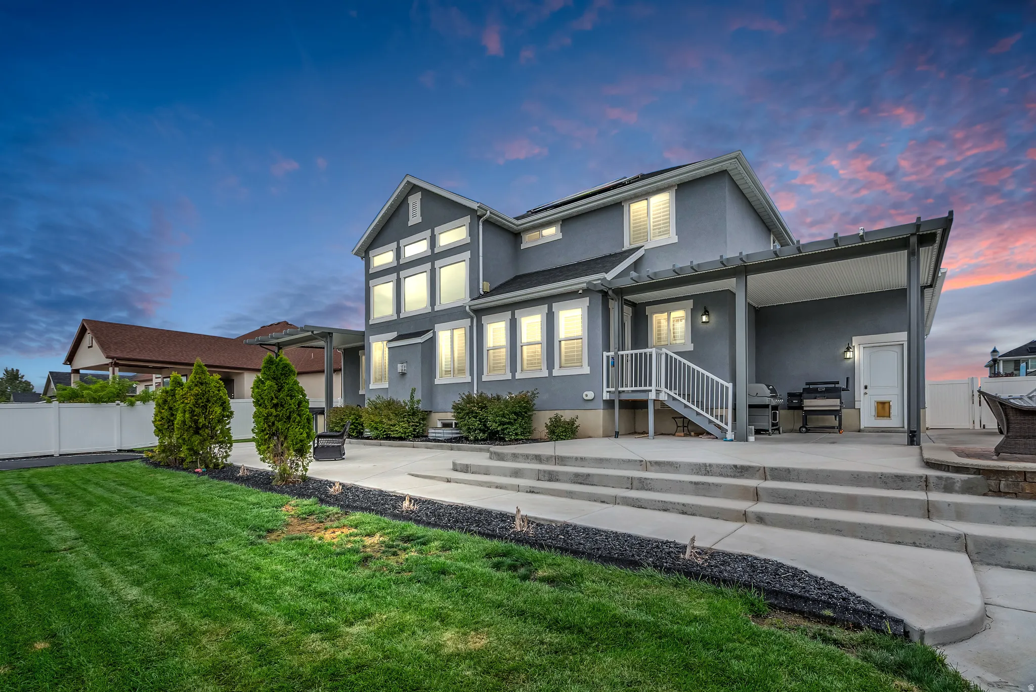 Expansive backyard featuring a manicured lawn, concrete patio with steps, and a covered pergola