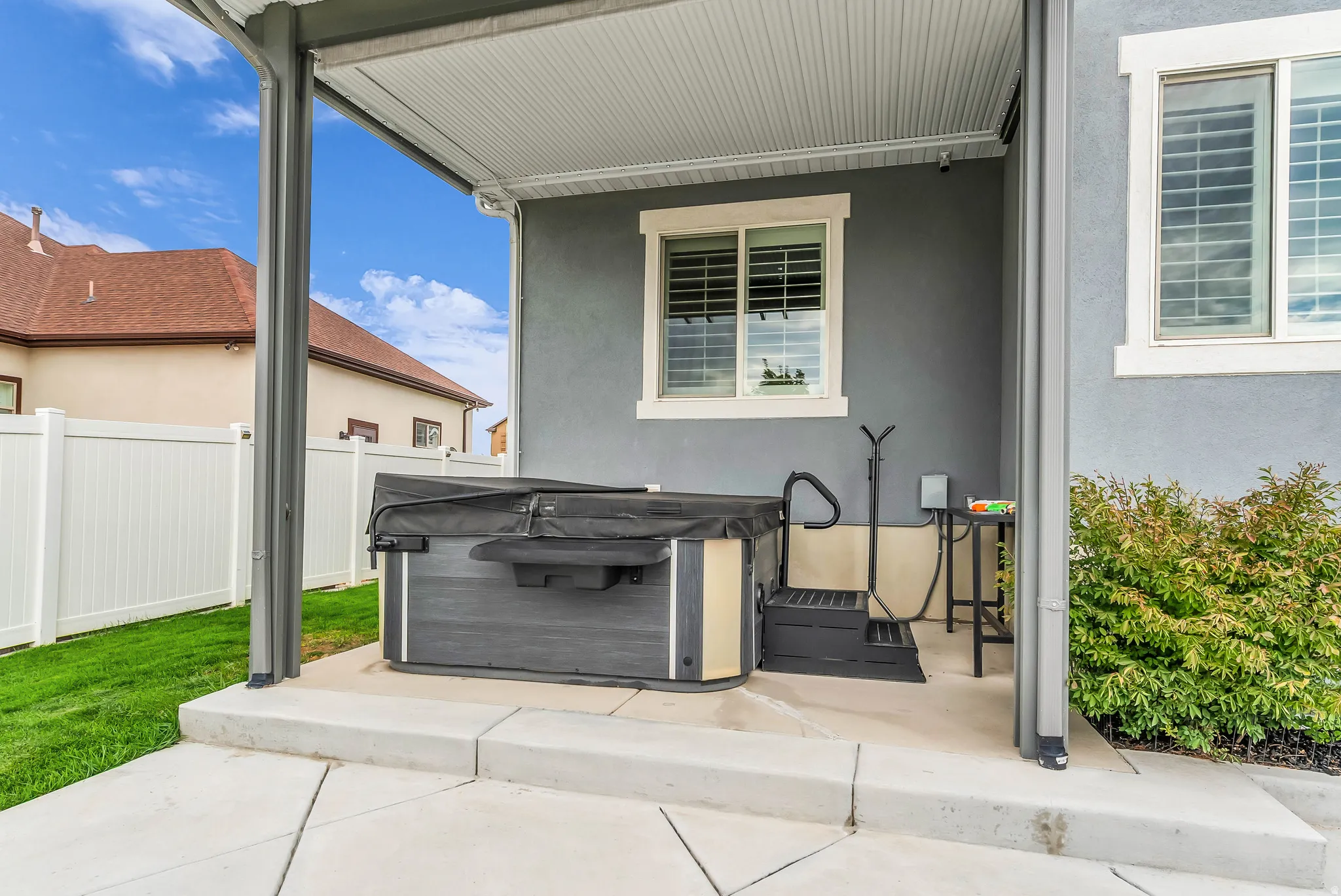 Covered patio area with a hot tub, steps, and privacy fencing
