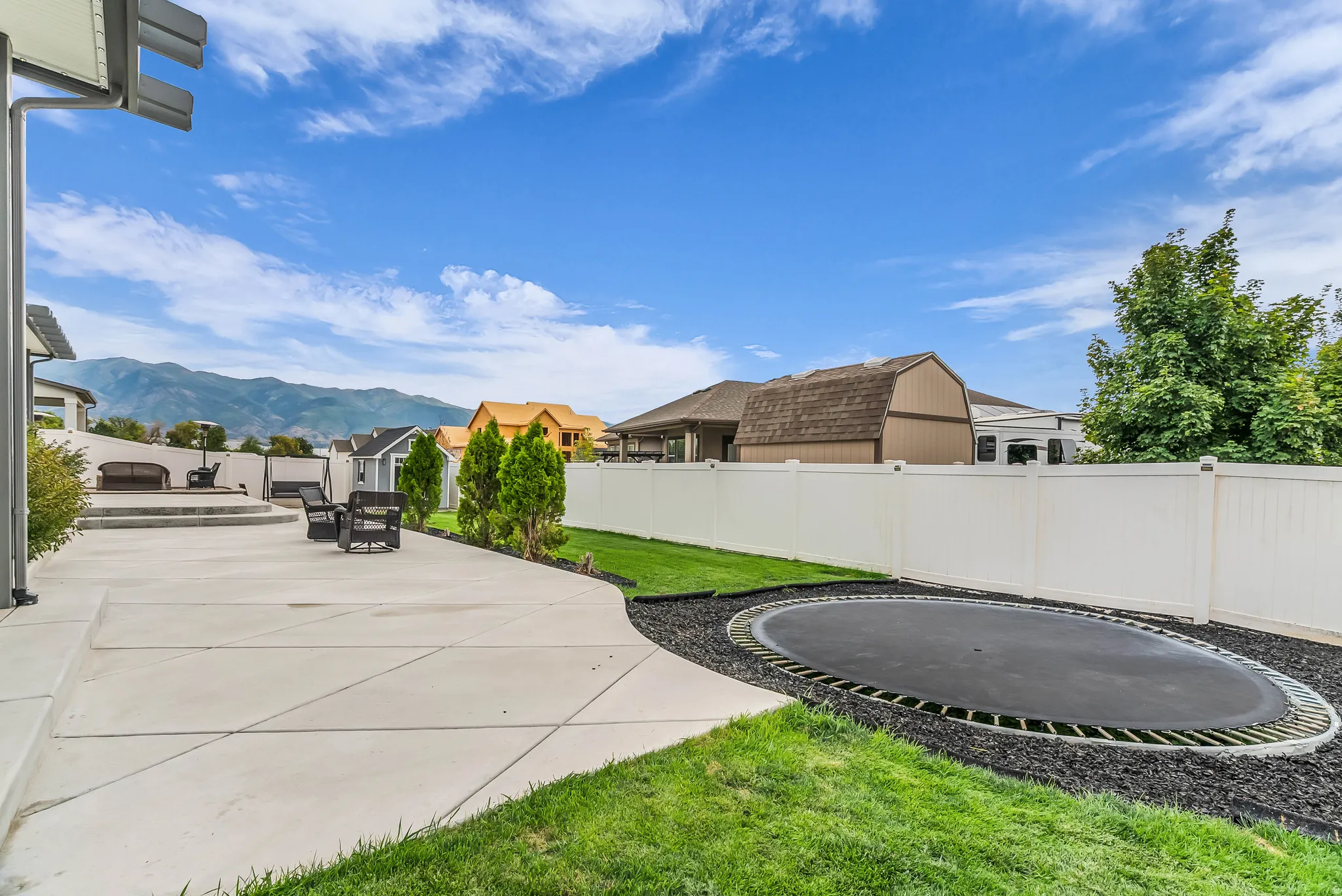 Expansive concrete patio with tiered levels, surrounded by a manicured lawn and a white privacy fence