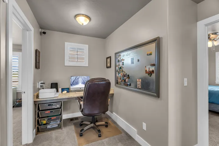 Built-in desk with a light-toned countertop, white window shutters, and carpeted flooring