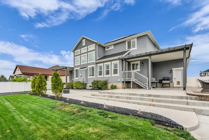 Expansive backyard featuring a large concrete patio, multi-level steps, a covered pergola, and a manicured lawn