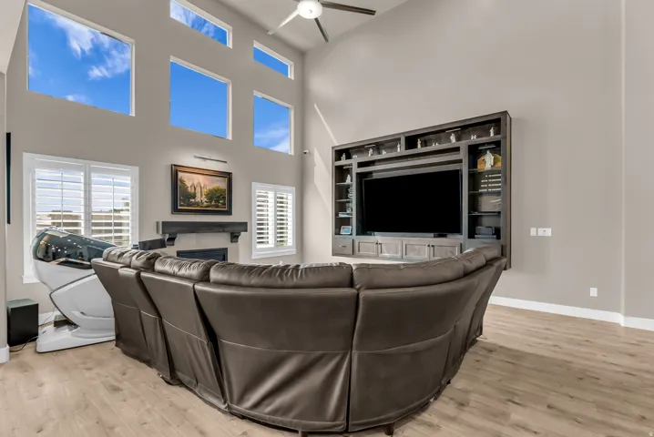 Living room featuring a vaulted ceiling with clerestory windows, wood-finish flooring, a built-in media center, and a fireplace with a wood mantle