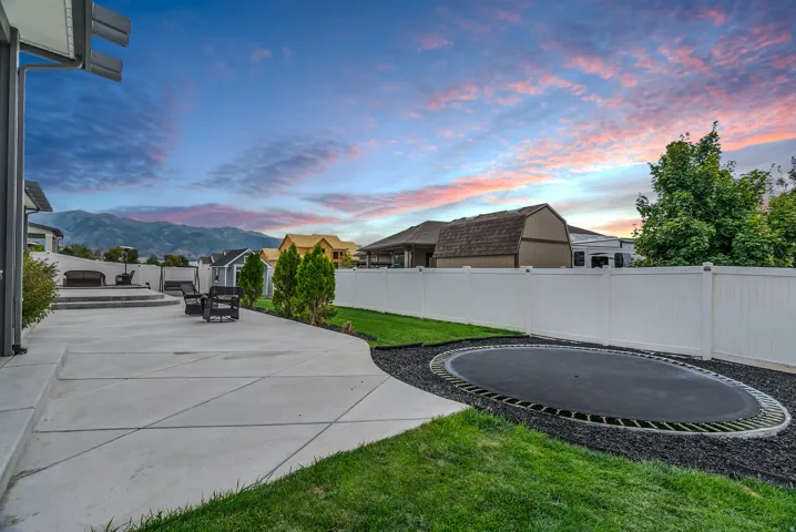 Expansive concrete patio with tiered sections, surrounded by a manicured lawn and a white privacy fence