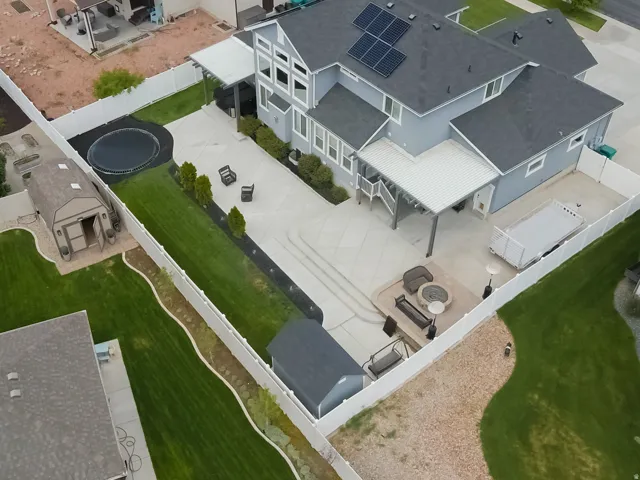 Expansive concrete patio with integrated fire pit area, covered outdoor living space, and solar panel array on roof