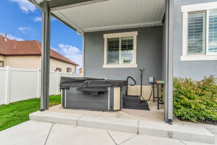 Covered patio area with a hot tub, steps, and privacy fencing