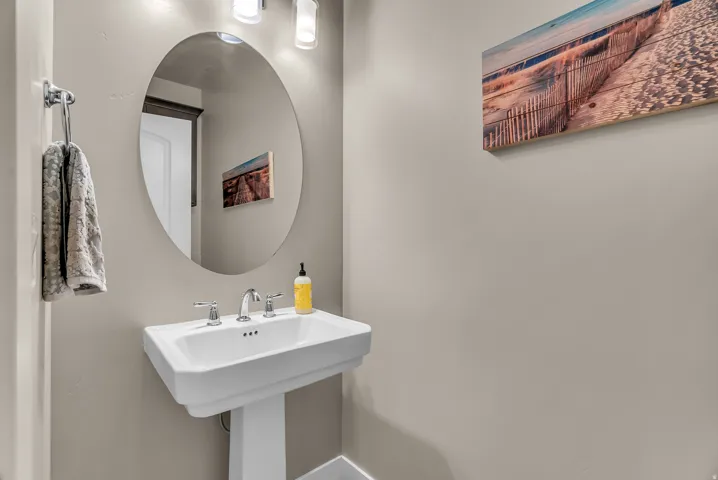 Pedestal sink with a chrome faucet, oval wall-mounted mirror, and an overhead light fixture
