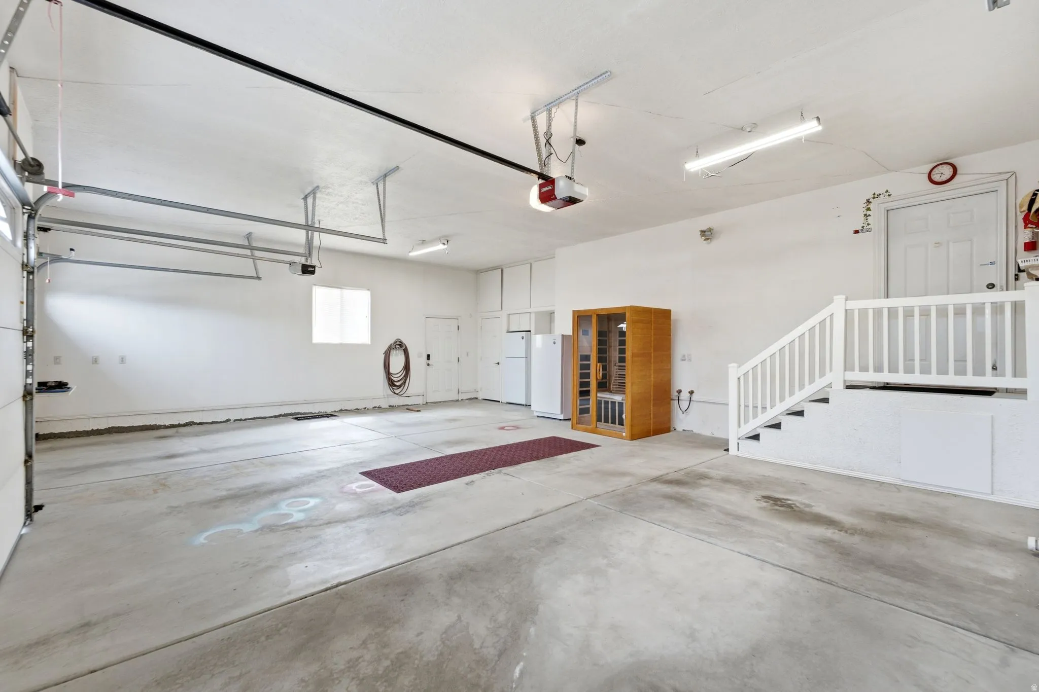 Spacious garage featuring a concrete floor, built-in storage cabinets, and a white painted staircase with a railing