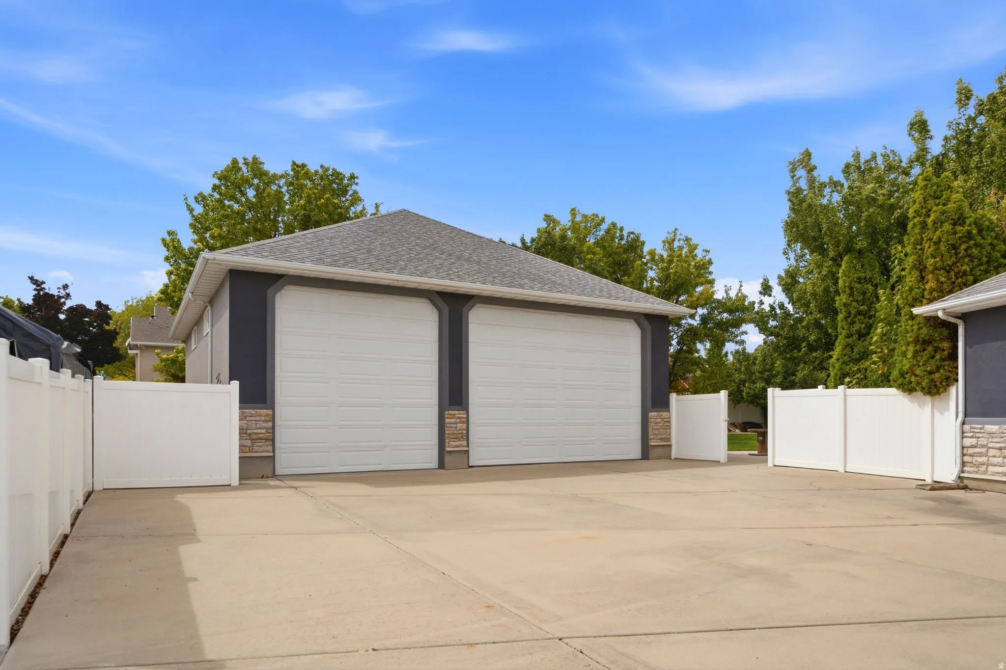 Detached two-car garage with white paneled doors, stone-finish accents, and a shingle roof