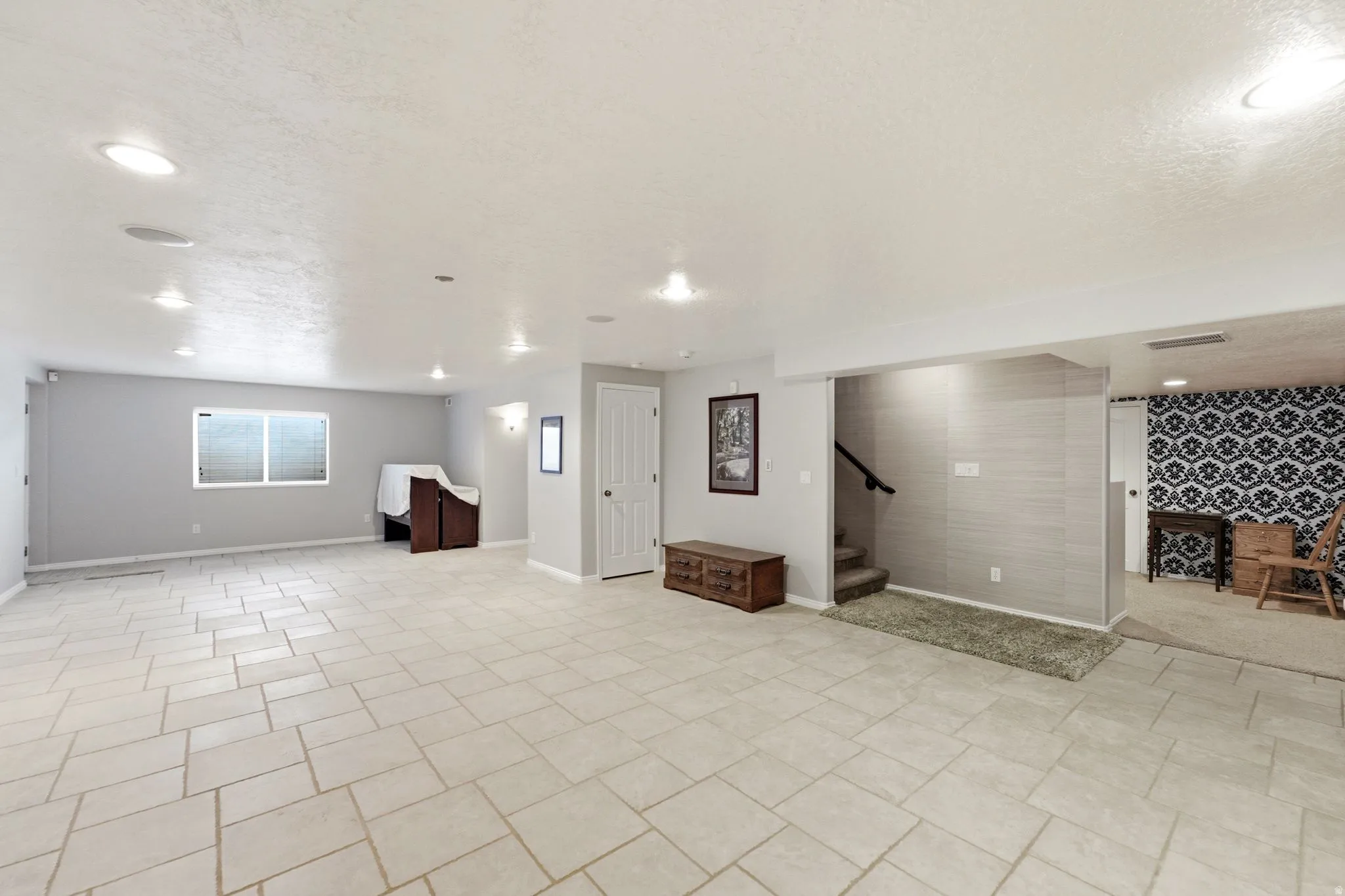 Expansive room with neutral tile flooring, recessed lighting, and a window with blinds