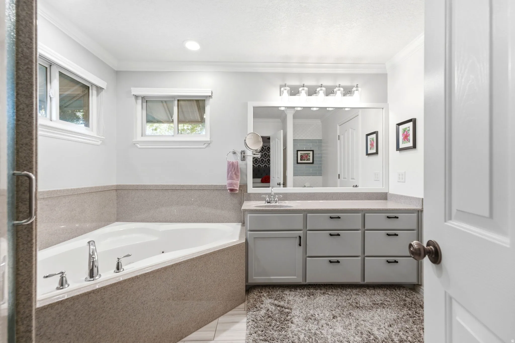 Built-in soaking tub with deck-mounted fixtures, dual windows, extended vanity with integrated sink, framed mirror, and multi-light vanity fixture