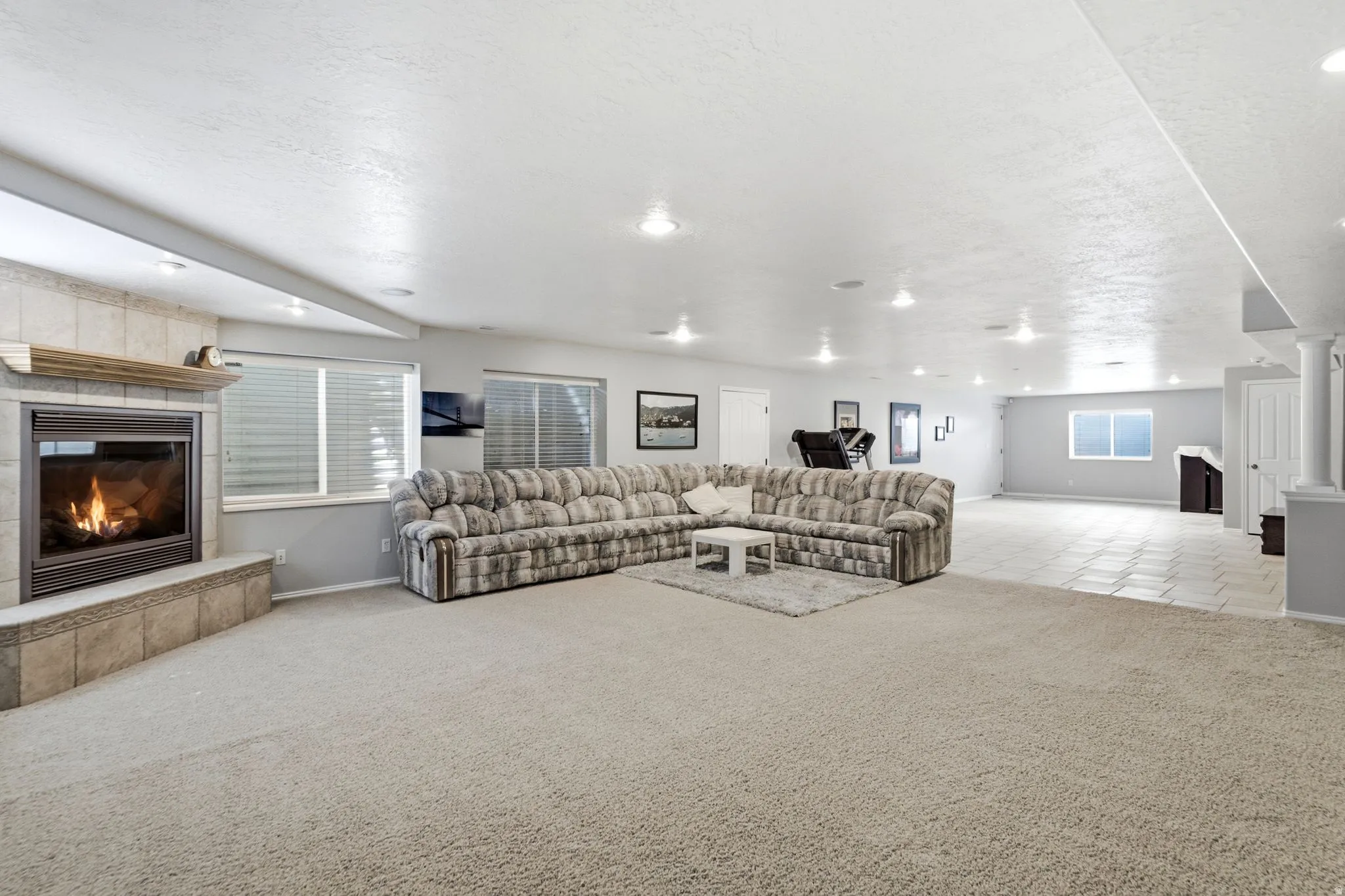 Spacious living area featuring carpet flooring, recessed lighting, a tile-surround fireplace with a wood mantel, and multiple windows