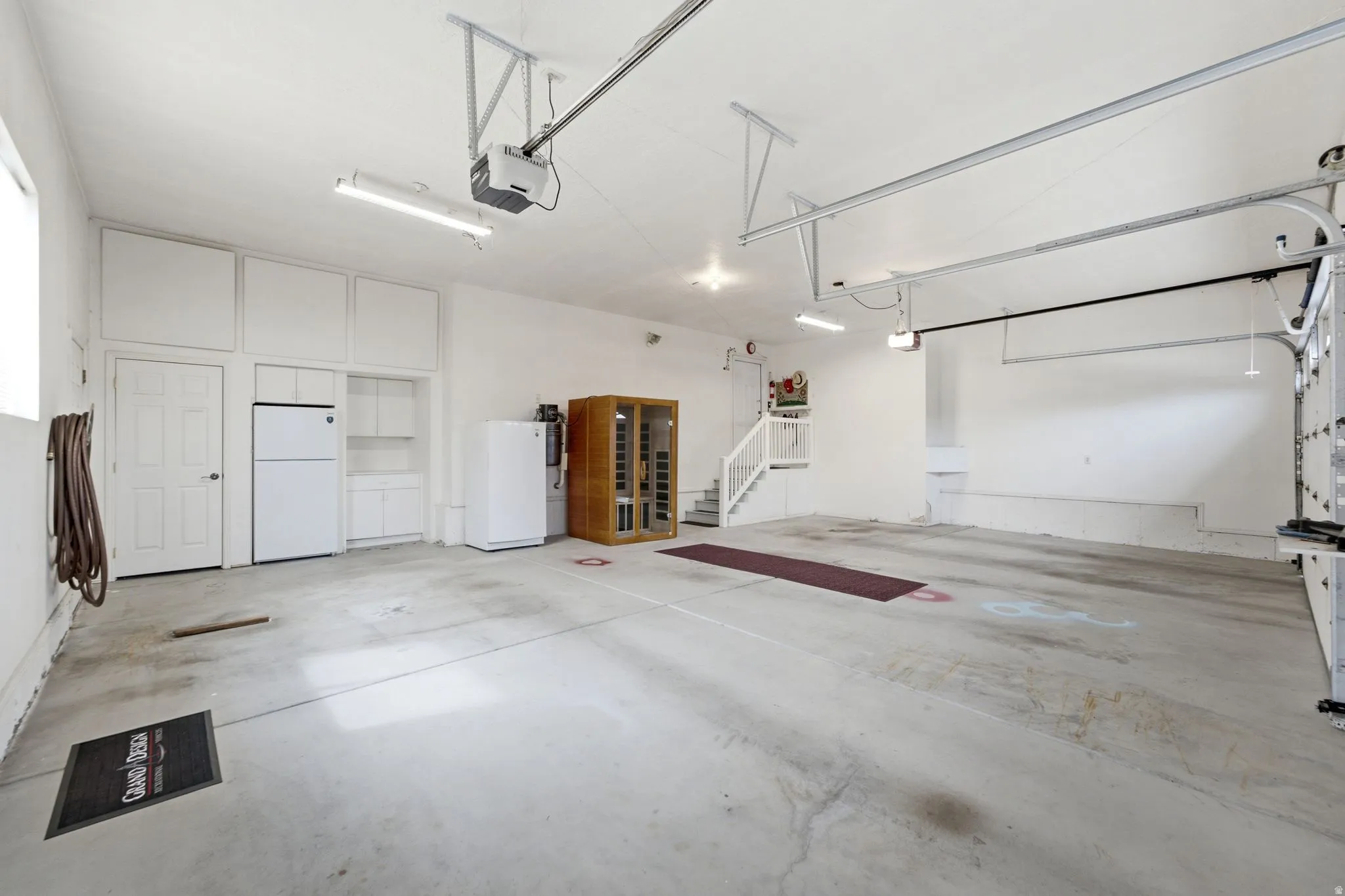 Spacious garage featuring concrete flooring, built-in cabinetry, an interior door, a staircase with railing, and fluorescent lighting