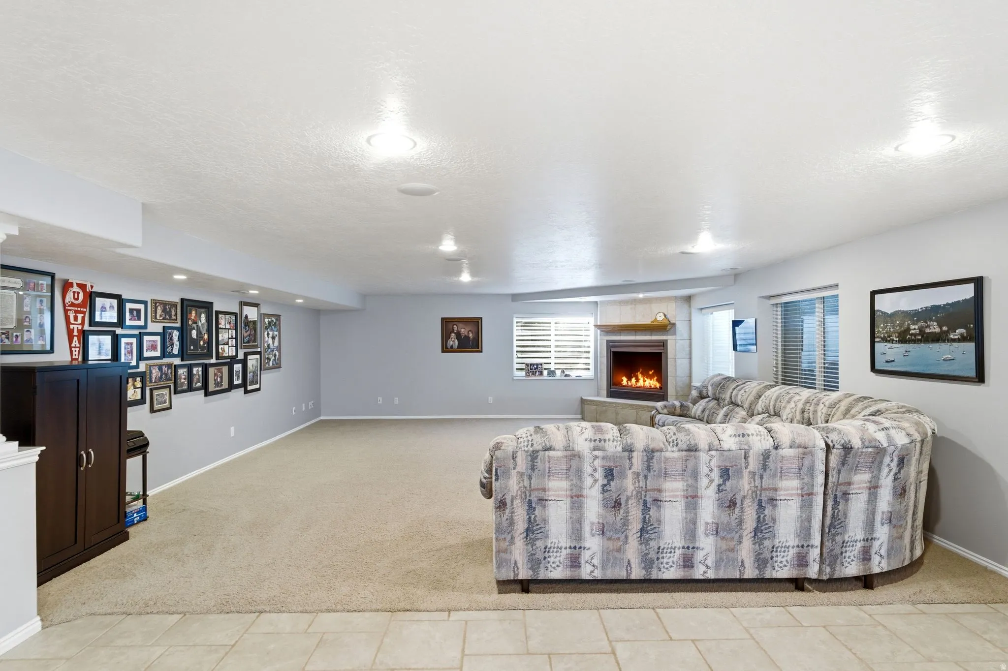 Spacious room featuring a corner fireplace with a tiled surround and mantel, recessed lighting, carpet flooring, and neutral wall tones