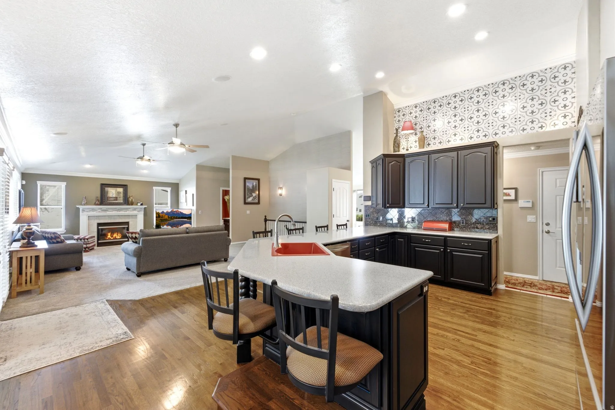 Hardwood flooring, kitchen island with seating, dark wood cabinetry, recessed lighting, and a fireplace with a stone mantel