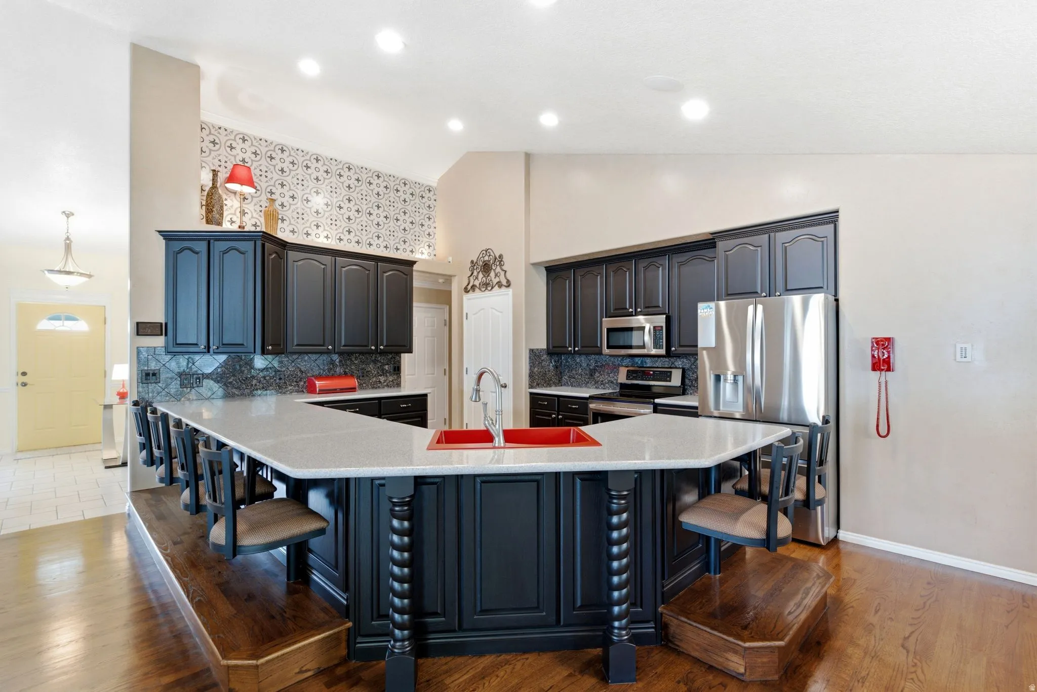 Kitchen featuring a large central island with seating, dark cabinetry, stainless steel appliances, and wood-finish flooring