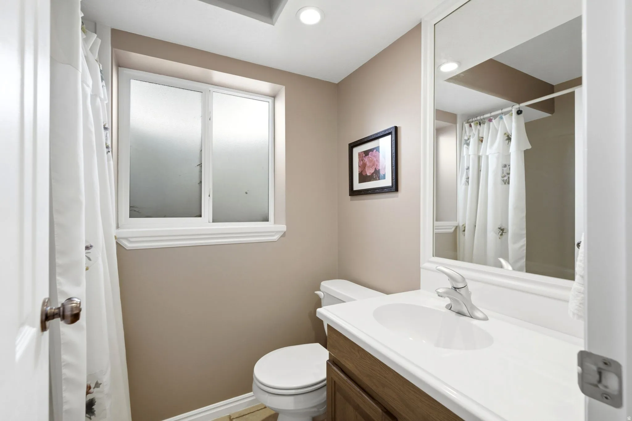 Bathroom featuring a window with frosted panes, a single-sink vanity with a white countertop, and a framed mirror