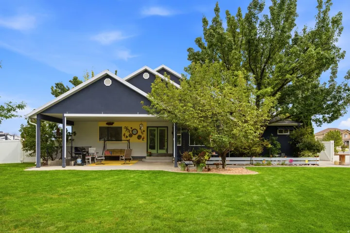 Expansive backyard featuring a lush lawn, mature trees, and a covered patio