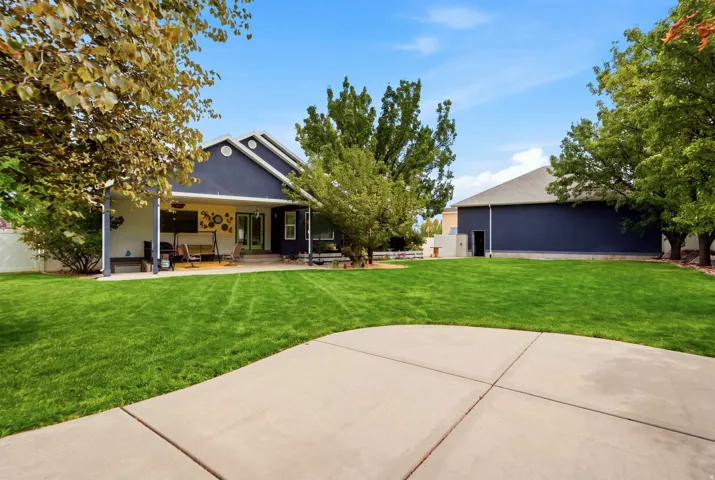 Expansive lawn with mature trees, covered patio, and concrete hardscaping