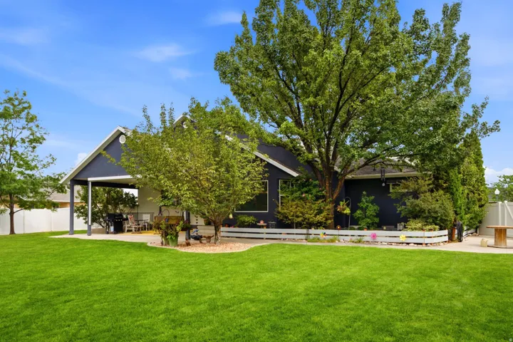 Expansive green lawn, mature trees, white privacy fence, covered patio, gravel landscaping