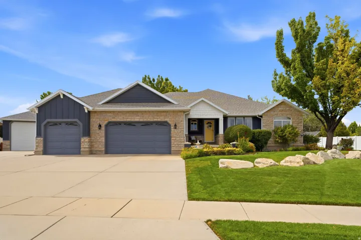 Stone and siding exterior with a multi-car garage, expansive concrete driveway, and a landscaped lawn with decorative boulders