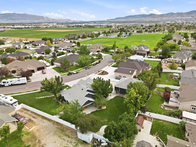 Aerial perspective of a residential neighborhood with green spaces, paved streets, and mountainous terrain in the background