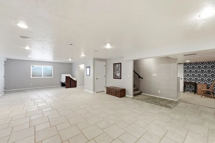 Expansive room with neutral tile flooring, recessed lighting, and a window with blinds