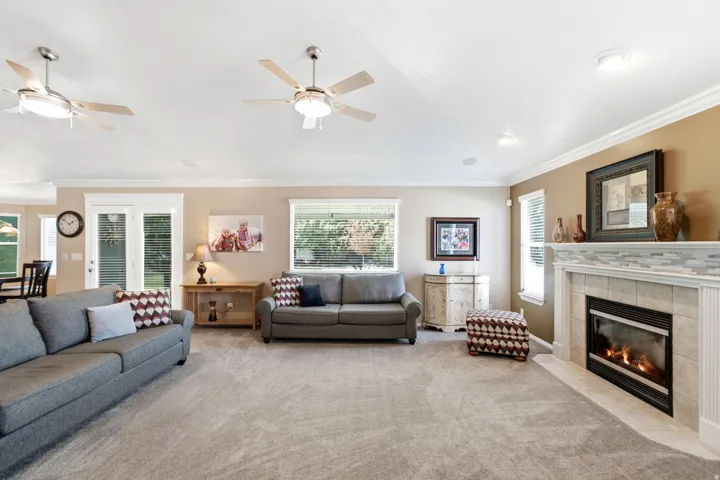 Living area featuring a tiled fireplace with decorative mantel, crown molding, double pane windows, and ceiling fans