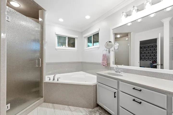 Frosted glass shower enclosure, corner soaking tub, dual windows, single vanity with light-toned countertop, and recessed lighting