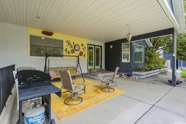 Covered concrete patio featuring an overhead pendant light, an exterior painted in grey and yellow hues, and a built-in planter box with established greenery