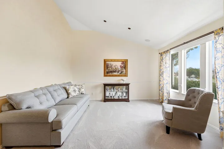 Vaulted ceiling with recessed lighting, large bay window, crown molding, and neutral carpeting