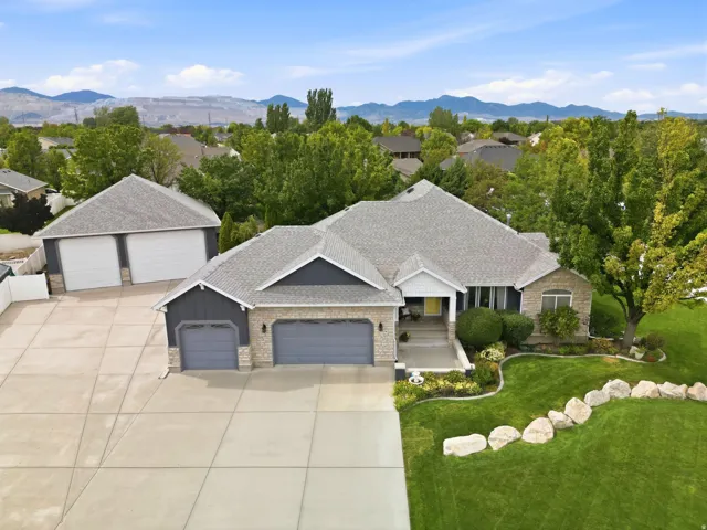 Stone and siding exterior with an attached two-car garage, separate two-car garage, expansive concrete driveway, mature landscaping, and mountain backdrop