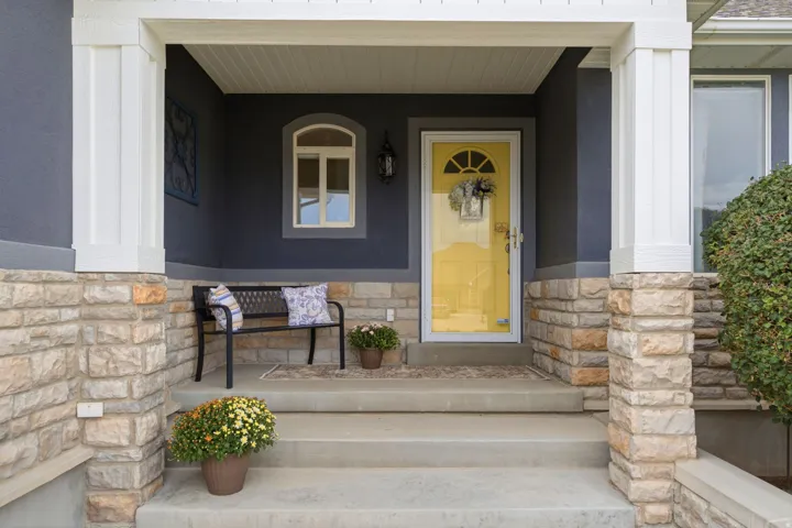 Covered porch with stone accents, a vibrant yellow entry door, and concrete steps