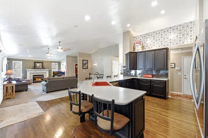 Hardwood flooring, kitchen island with seating, dark wood cabinetry, recessed lighting, and a fireplace with a stone mantel