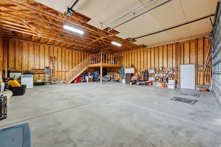 Spacious garage featuring a concrete floor, exposed wood framing, an interior staircase to a mezzanine, and a roll-up garage door