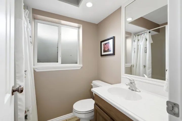 Bathroom featuring a window with frosted panes, a single-sink vanity with a white countertop, and a framed mirror