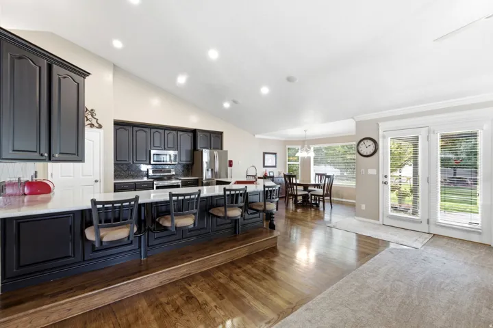 Vaulted ceilings, dark wood-finish cabinetry, stainless steel appliances, breakfast bar with seating, and wood-finish flooring