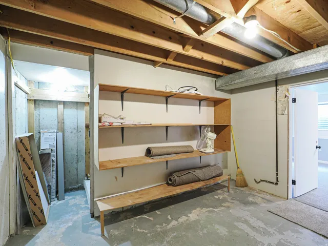 Built-in wood shelving, exposed ceiling joists, overhead lighting, concrete flooring, and an interior doorway