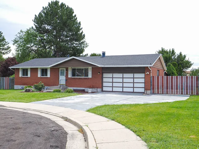 Brick exterior with white window shutters, a two-car garage, a concrete driveway, and a front lawn