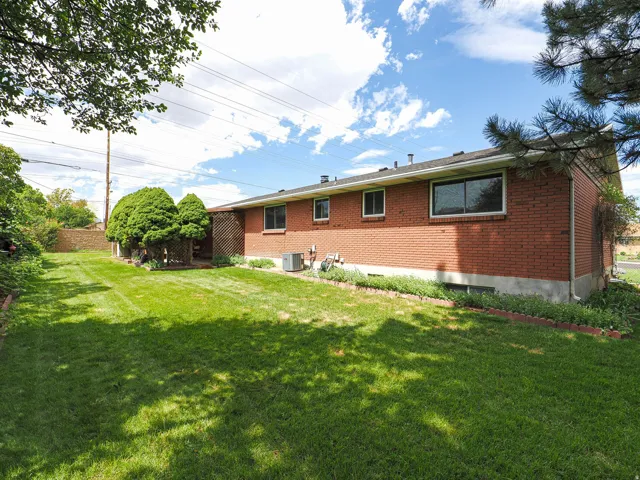 Expansive rear yard featuring a green lawn, brick exterior, multiple windows, and mature perimeter trees