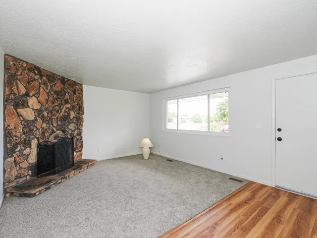 Stone-clad fireplace with hearth, carpeted flooring, wood-finish flooring, white walls, and a large window