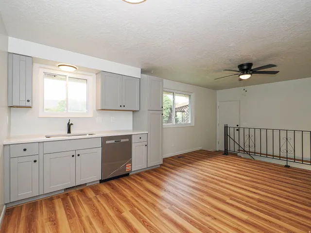 Kitchen area featuring light gray cabinetry, a stainless steel dishwasher, a single basin sink with a matte black faucet, and wood-finish flooring