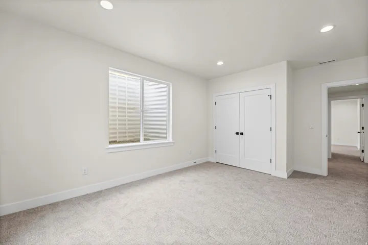 Recessed lighting, light-colored carpeting, white interior walls, white window trim, and bi-fold closet doors with matte black hardware