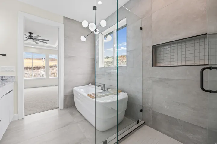 Spacious bathroom featuring a freestanding soaking tub, glass-enclosed shower, large format tile flooring, a window, and a modern light fixture