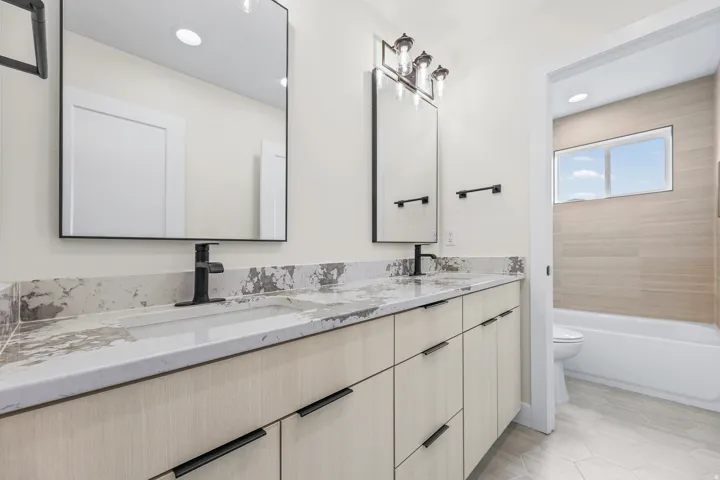 Dual vanity with integrated sinks, light wood-finish cabinetry, matte black hardware, and rectangular mirrors
